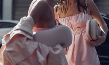 Sokak stili, soluk pembe kolsuz bluz dizli, işlemeli, soluk pembe bir midi elbise giyen bir kadın, soluk pembe, büyük boy, uzun bir trençkot ve pembe kayışlı sandaletler..