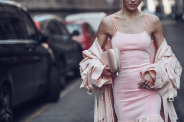 Sokak stili, soluk pembe kolsuz bluz dizli, işlemeli, soluk pembe bir midi elbise giyen bir kadın, soluk pembe, büyük boy, uzun bir trençkot ve pembe kayışlı sandaletler..