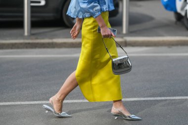 Milan, Italy - February, 24: Street style, woman wearing Prada outfit: blue V-neck bra, a matching blue cropped bomber coat, yellow midi skirt and silver pointed pumps heels shoes. clipart