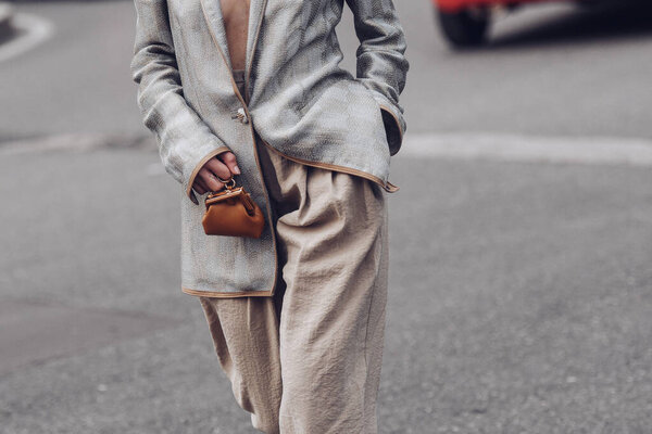 Milan, Italy - February, 24: Street style, woman wearing silver blazer jacket, beige large pants, a brown shiny leather micro First handbag from Fendi, white leather with large silver buckle heels.