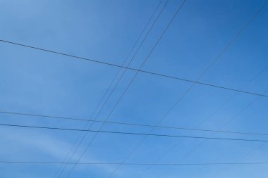 Mavi gökyüzünün arka planında yüksek gerilim kablolarından oluşan bir ağ..