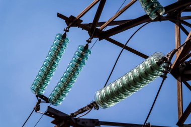 Mavi gökyüzüne karşı yüksek voltajlı elektrik hatları ve ekipmanlar.