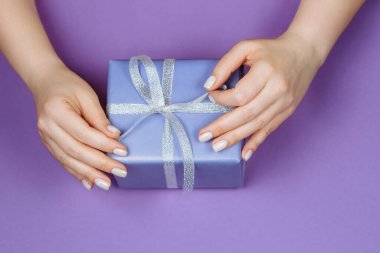 Elinde gümüş bir kurdele ve mor bir arka planda Noel manikürü olan bir hediye.