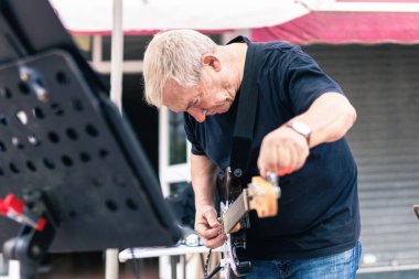Sahnede elektro gitarını akort eden yaşlı müzisyen.