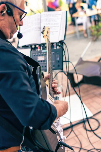 Starszy muzyk gra na gitarze elektrycznej na tarasie z publicznością — Zdjęcie stockowe