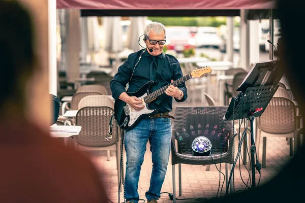 Yaşlı erkek müzisyen halka açık bir terasta elektro gitar çalıyor.