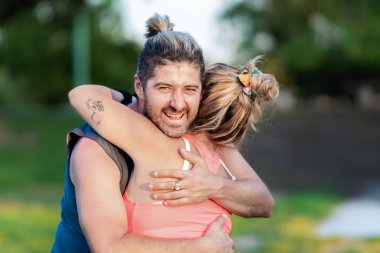 Parkta bir kadını kucaklarken gülümseyen sporcu adam.