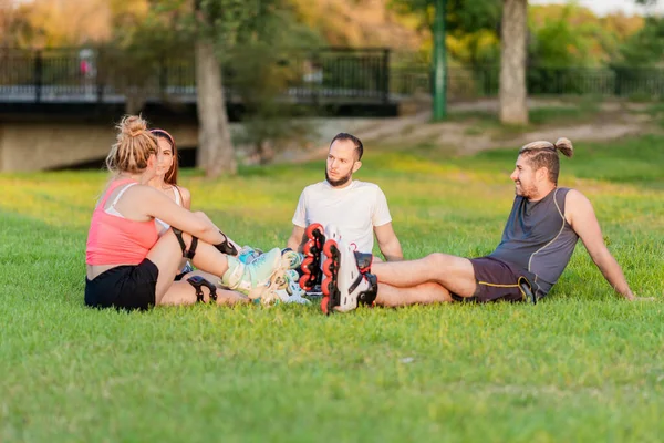 Группа друзей, сидящих в кругу в парке со встроенными коньками — стоковое фото