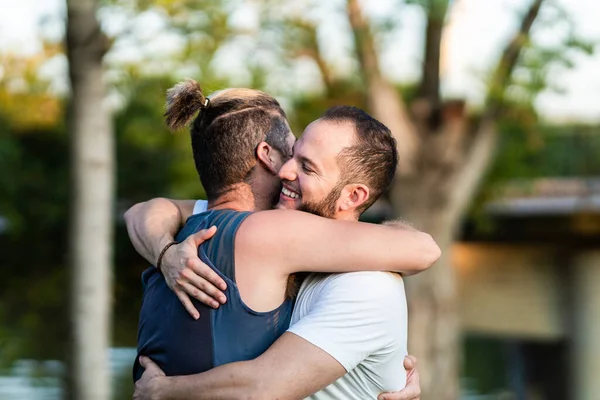 Чоловіки обіймаються, посміхаючись у парку — стокове фото
