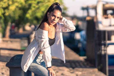 Arka planda kentsel manzarayla otururken poz veren genç bir kadın