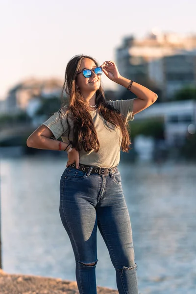 Молода біла жінка з сонцезахисними окулярами, що стоять біля річки під час заходу сонця — стокове фото
