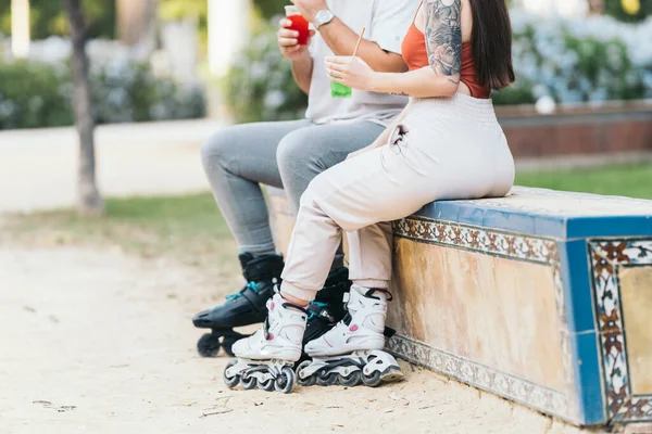 Dos personas que usan patines en línea sentadas al aire libre mientras beben bebidas coloridas — Foto de Stock