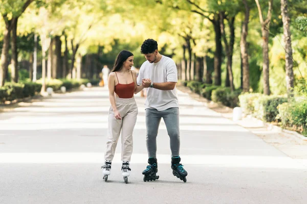 Молодий чоловік допомагає навчитися кататися на ковзанах жінці в громадському парку — стокове фото