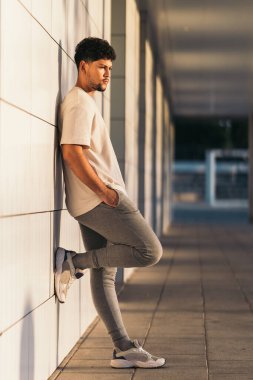 Gün batımında binanın ön cephesine yaslanmış bir adamın dikey fotoğrafı.