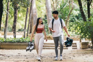 Parkta ellerinde patenlerle yürüyen gençler.