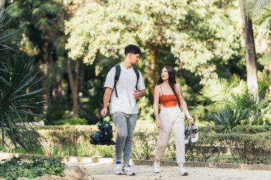 Parkta ellerinde patenlerle yürüyen iki genç insan.