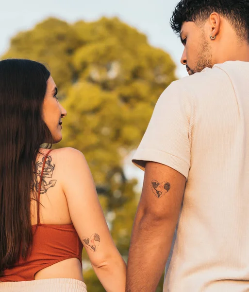 在公园里手牵着手，手臂上有同样纹身的情侣 — 图库照片