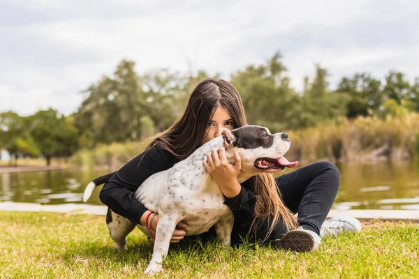 Jovem mulher beijando um cão enquanto se senta ao lado de um rio — Fotografia de Stock