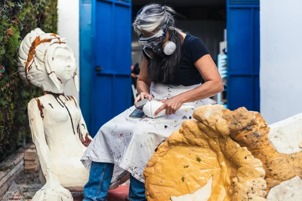 Женщина защищена маской, работающей над скульптурой из полистирола в саду — стоковое фото