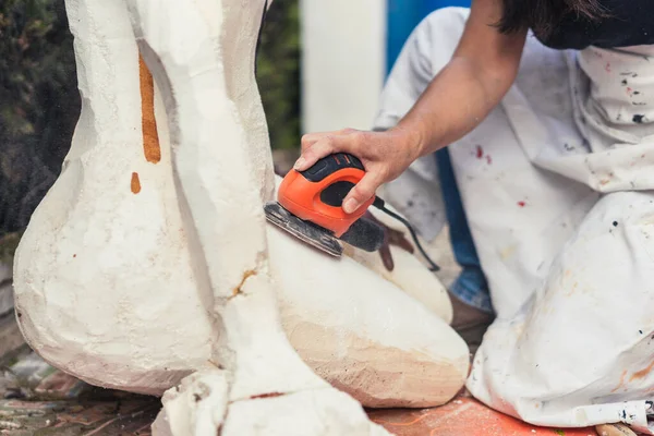 Woman using an electric polisher on a polystyrene figure outdoors — Stock Photo, Image