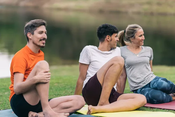 Расслабленная группа друзей, сидящих на коврике для йоги в парке — стоковое фото