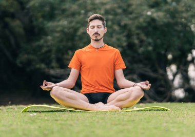 Nilüfer yogası yapan bir adam açık havada minder üzerinde poz veriyor.