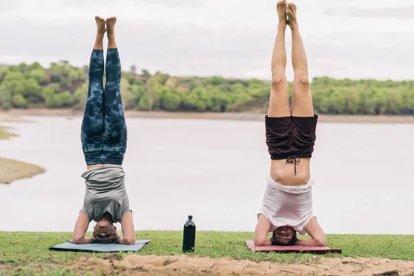 Два человека с головой на полу практикуют йогу в парке с озером — стоковое фото