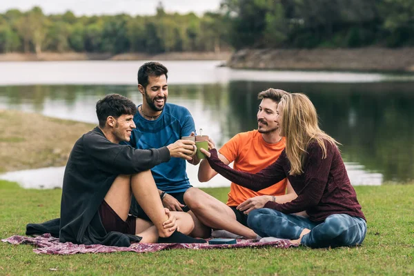 Skupina přátel ve sportovním oblečení toasting s čajem při posezení v parku — Stock fotografie