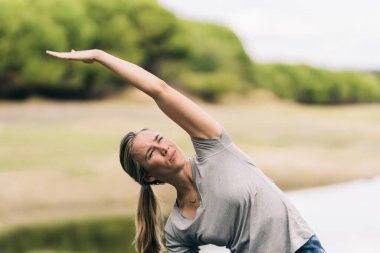 Kadın parkta yoga yaparken sırtını esnetiyor.