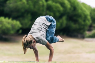 Sarışın kadın parkta yoga pozisyonu yapıyor.