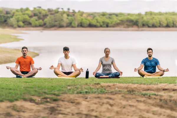 Vier mensen zitten tijdens het doen van de lotuspositie van yoga naast een meer — Stockfoto