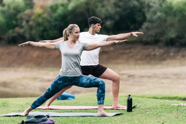 Блондинка и атлетичный мужчина в спортивной одежде позируют для йоги в парке — стоковое фото