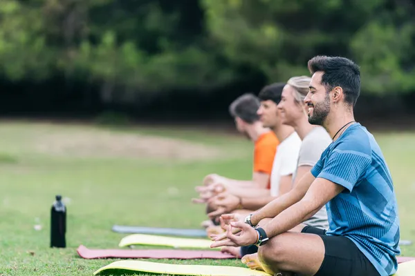 Gülen insanlar parkta yoga pozu veriyorlar.
