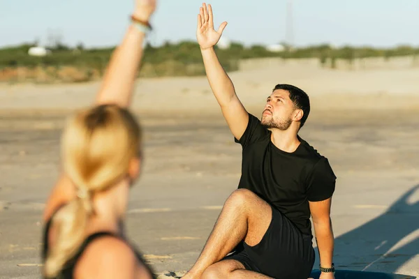 Человек изюм руку во время занятий йогой рядом со своим тренером на пляже — стоковое фото