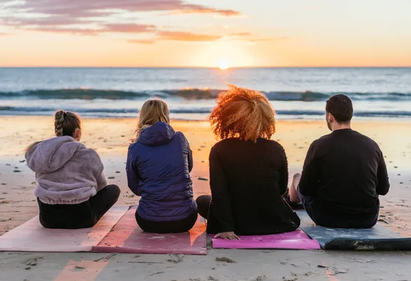 Multiethnic people sitting on yoga mats facing the sea horizon during sunset