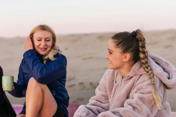 Duas mulheres loiras conversando enquanto bebem chá sentado em uma praia — Fotografia de Stock