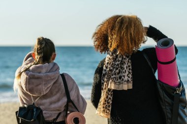 İki etnik çeşitliliğe sahip kadının sırtında yoga minderleri ve çantalar var.
