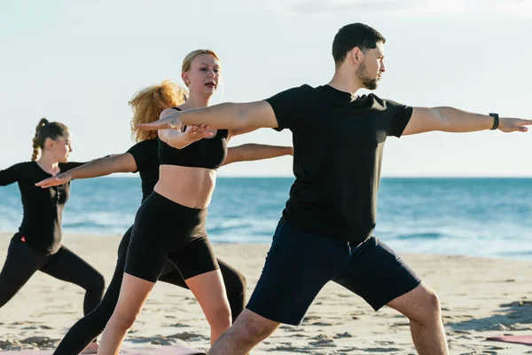 Инструктор по йоге исправляет позу человека во время занятий йогой на пляже — стоковое фото