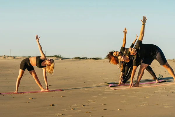 Тренер по йоге и группа мультиэтнических учителей, занимающихся йогой на пляже — стоковое фото