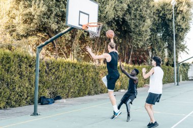 Uzun boylu bir adam arkadaşlarıyla basketbol oynarken basket oynamak için sepetin içine atlıyor.