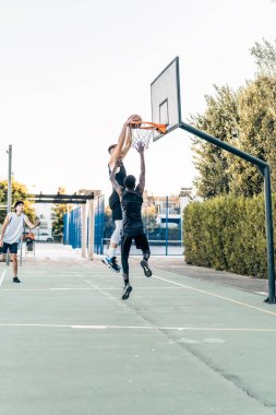Dış sahada oynanan bir basketbol maçında gol atan uzun boylu bir adam.