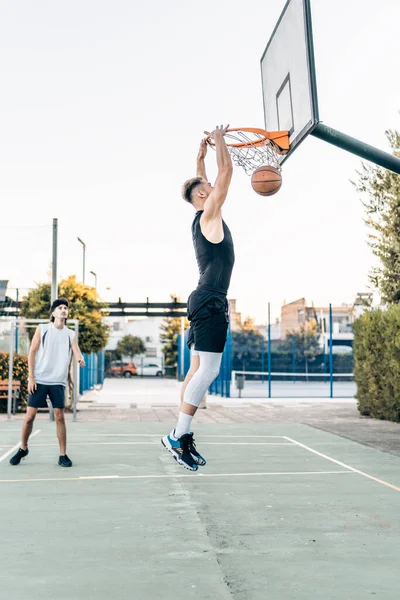 Dışarıda oynanan dostça bir basketbol maçında basket atan bir adam.