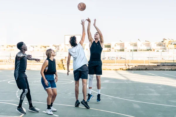 Gruppo di amici che saltano come giocare a basket in un campo all'aperto — Foto Stock