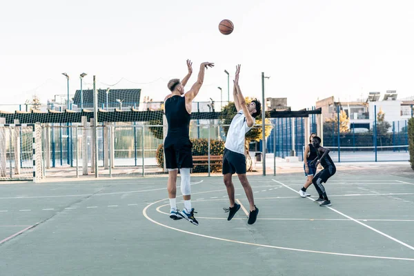 Amici che saltano mentre giocano a basket tra amici in un campo urbano all'aperto — Foto Stock