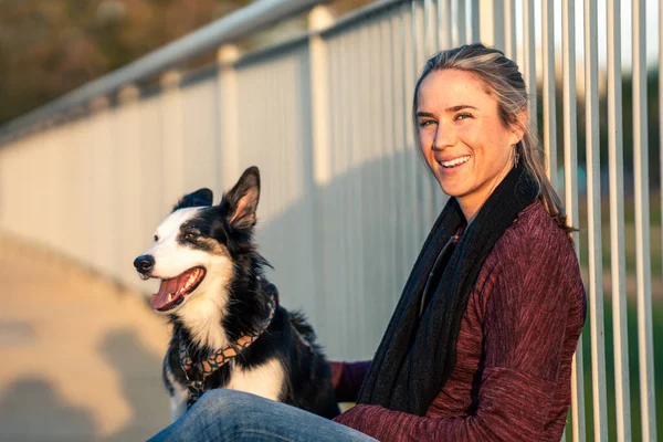Woman looking to the camera while petting a dog leaning on a bridge outdoors — Foto Stock