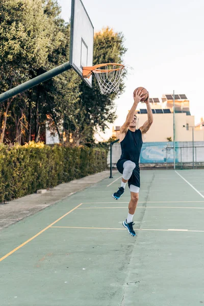 Vertical photo of a tall caucasian man jumping while shooting a ball in a basket — Foto Stock