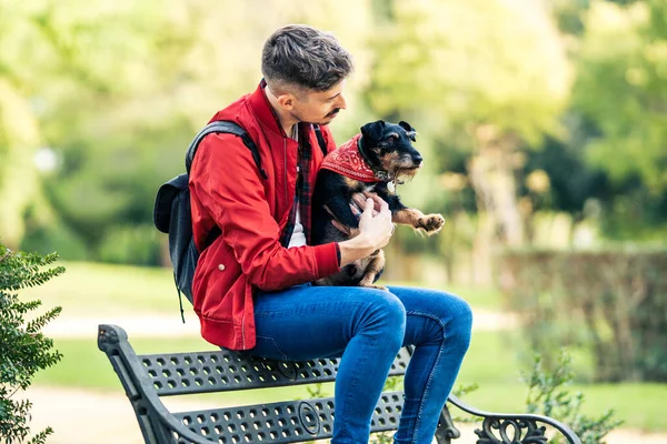 Människan omfamnar en liten hund sittande på en bänk i en park — Stockfoto