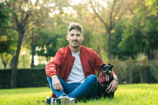 Yaşlı bir köpeğin yanında çimde oturan adamın dili dışarı çıkmış.
