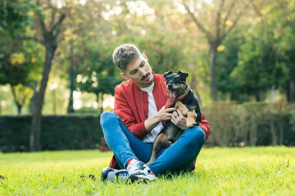 Homem sentado na grama acariciando um cão em um parque — Fotografia de Stock