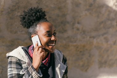 Young afro woman talking to the mobile while smiling outdoors